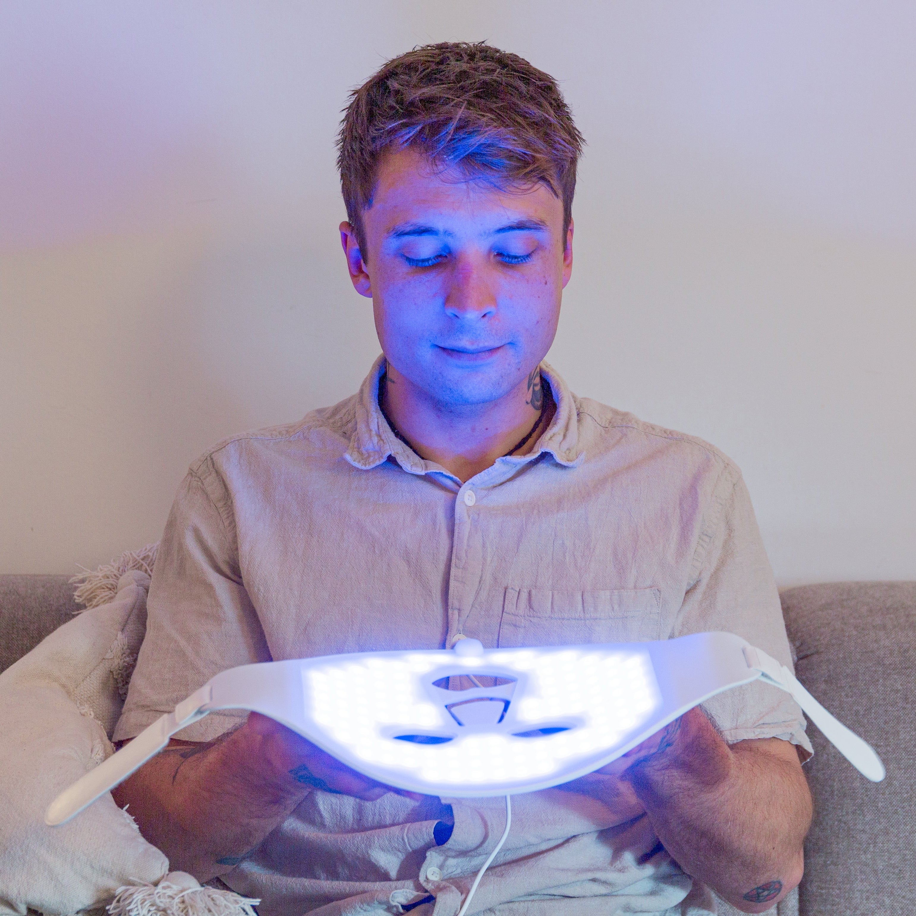 Person holding a glowing light therapy mask device on a couch