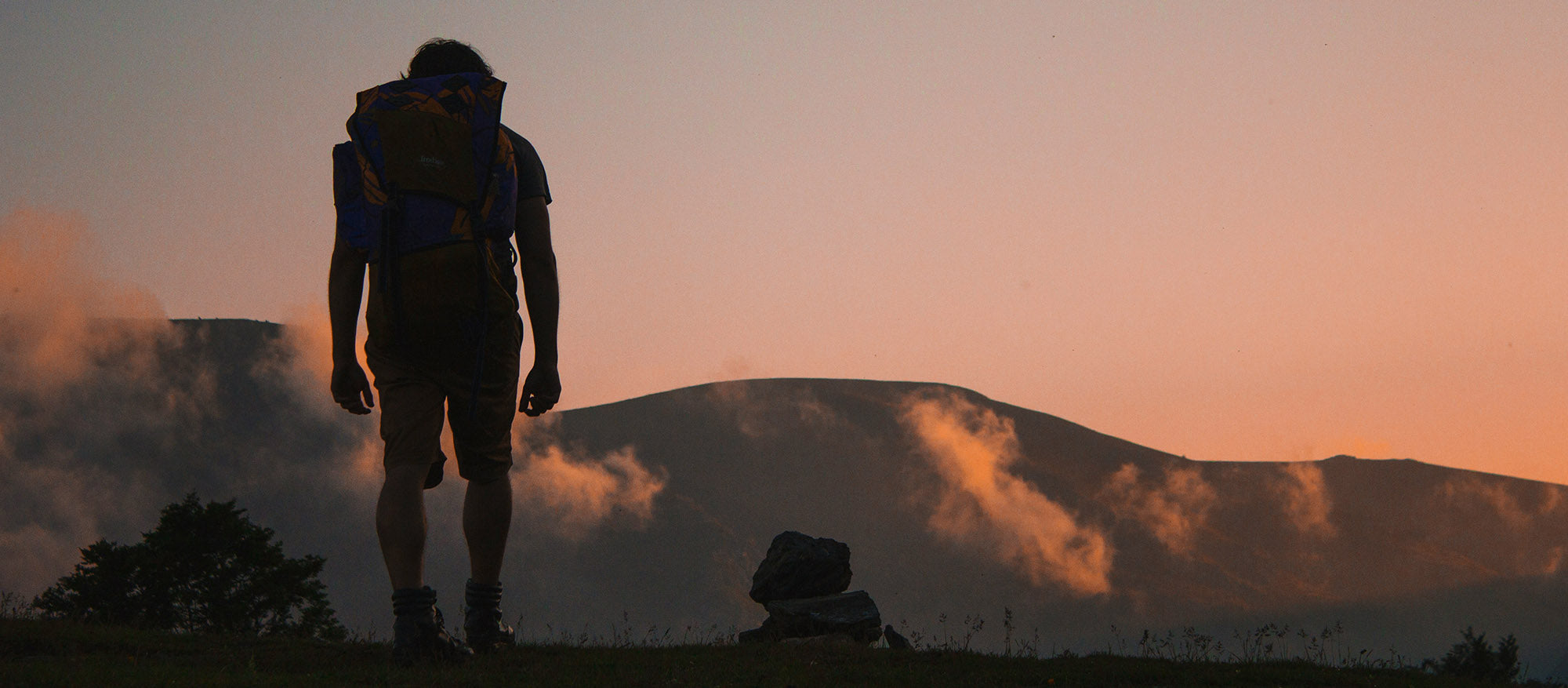 Person med ryggsekk ser utover fjellandskap i solnedgang – symbol på utforskning, vitenskap og Forge sin fremtid innen longevity