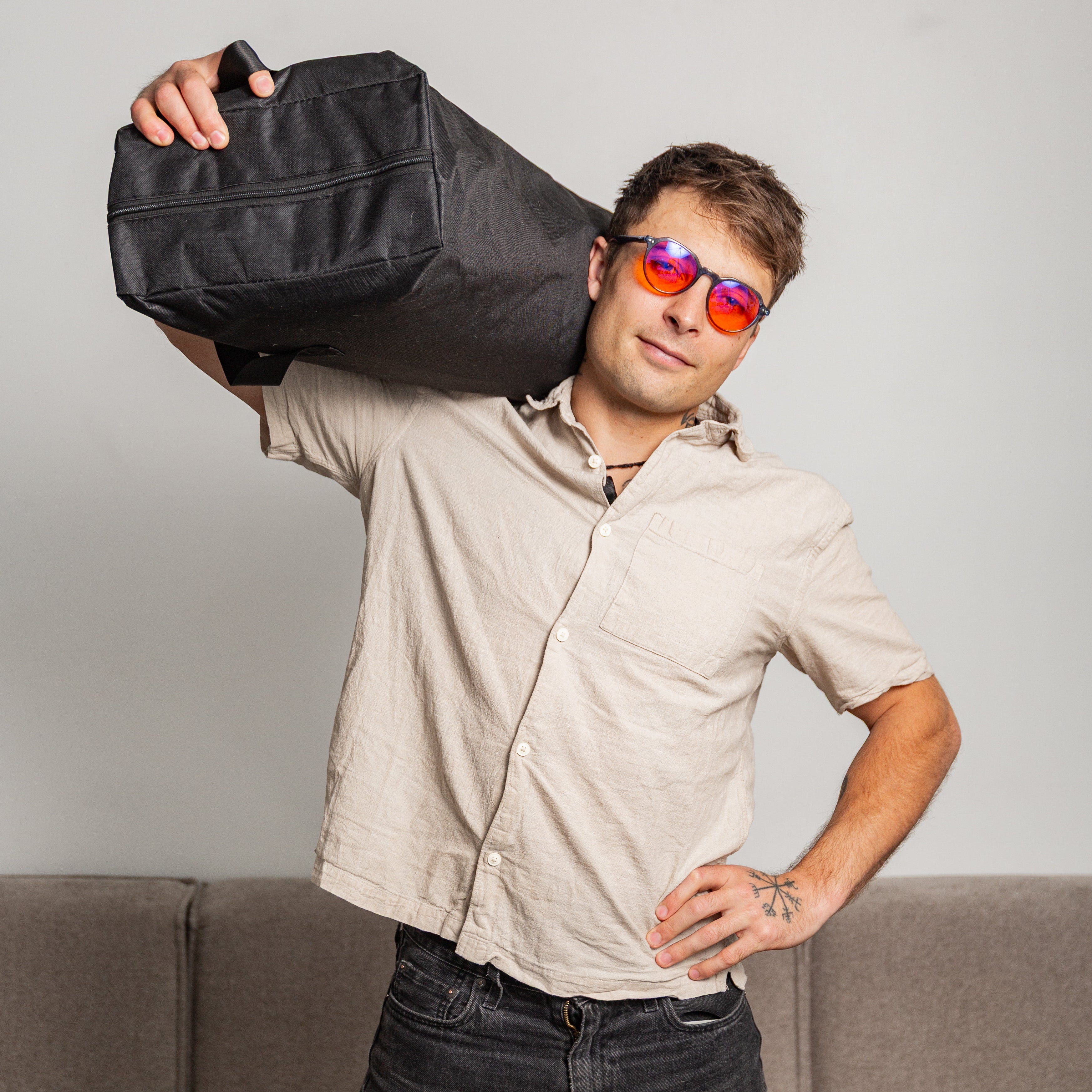 Man holding a black bag with a red light therapy blanket inside  over his shoulder with a neutral background
