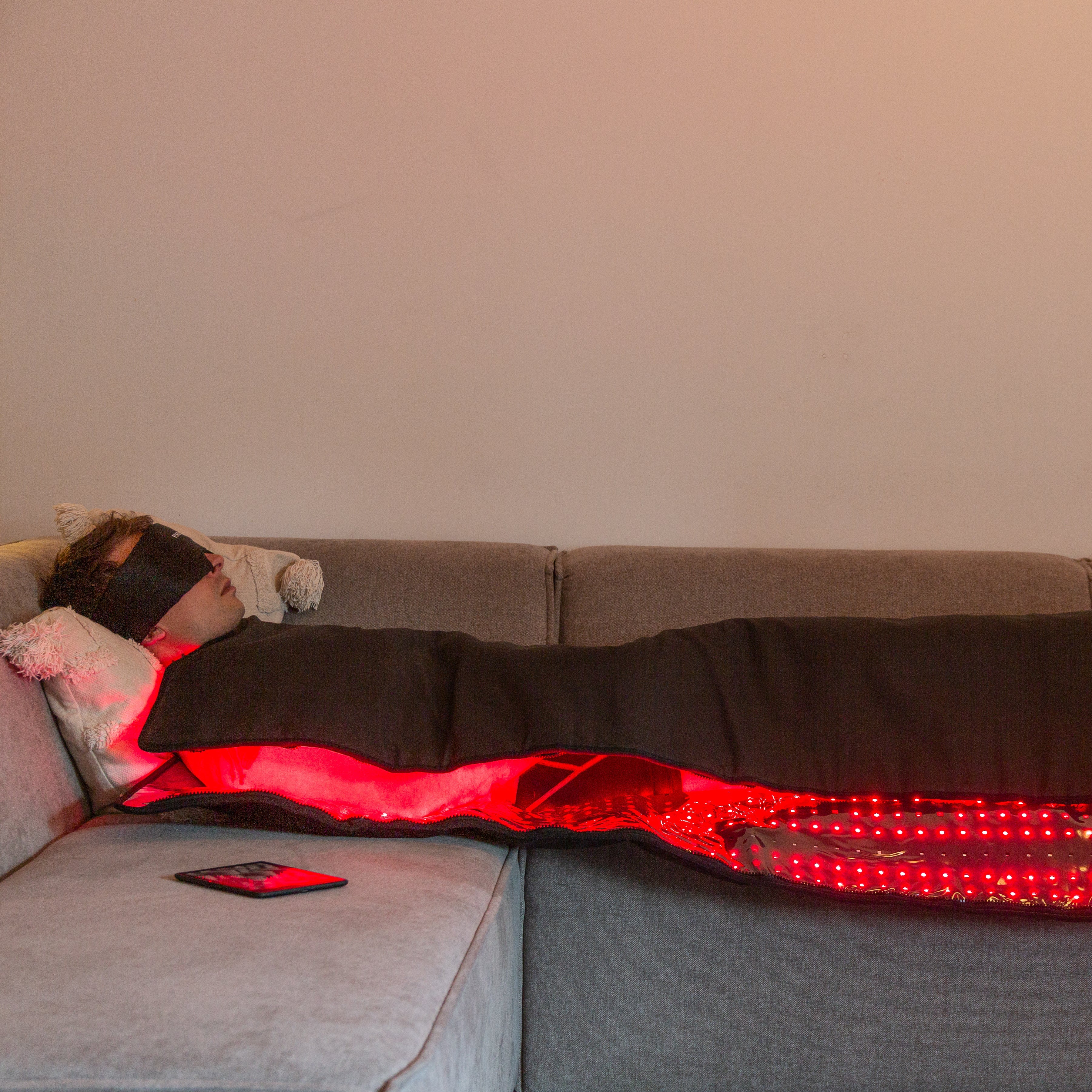 Person lying on a couch with a red light-emitting blanket