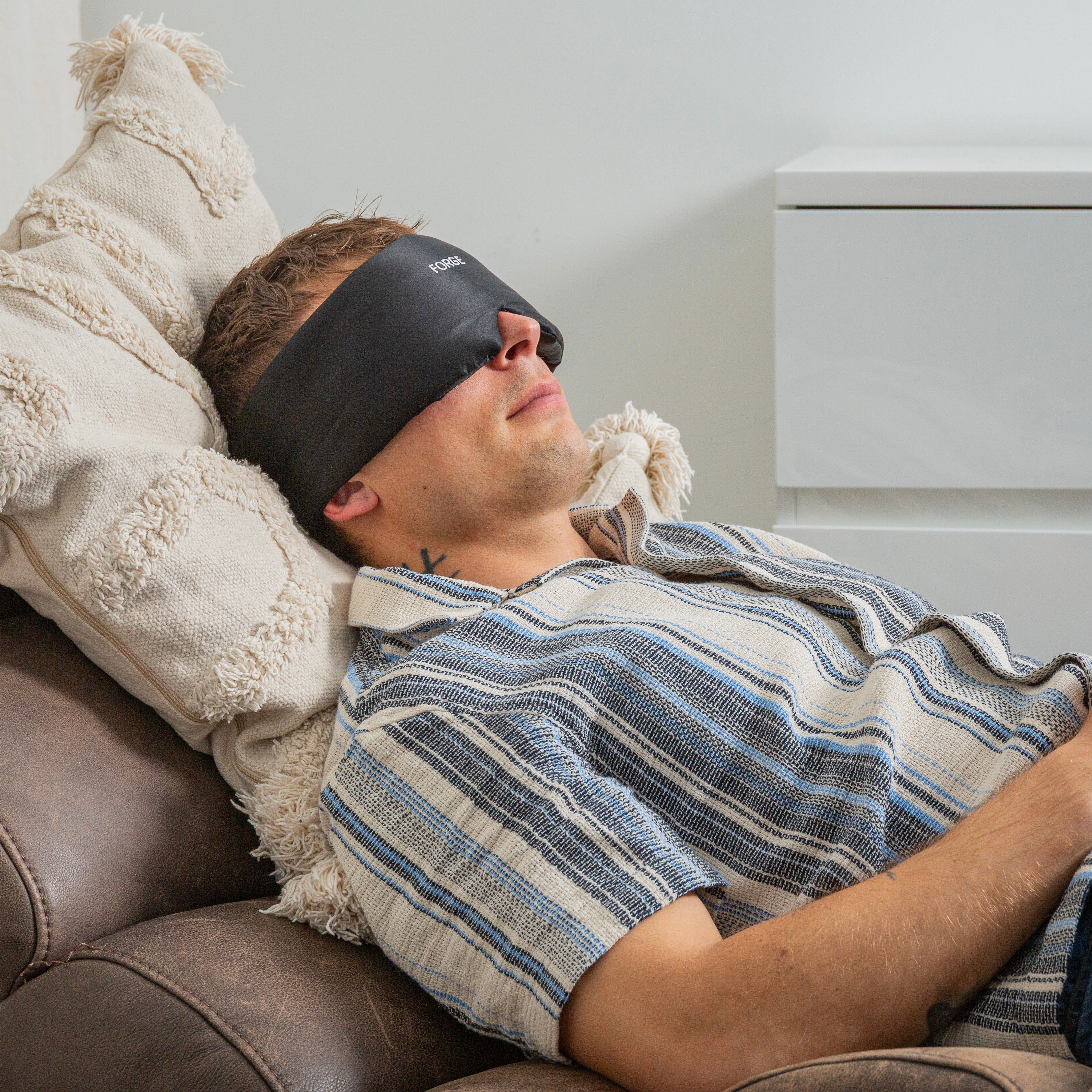 Man wearing a sleep mask and striped shirt, lying on a couch.