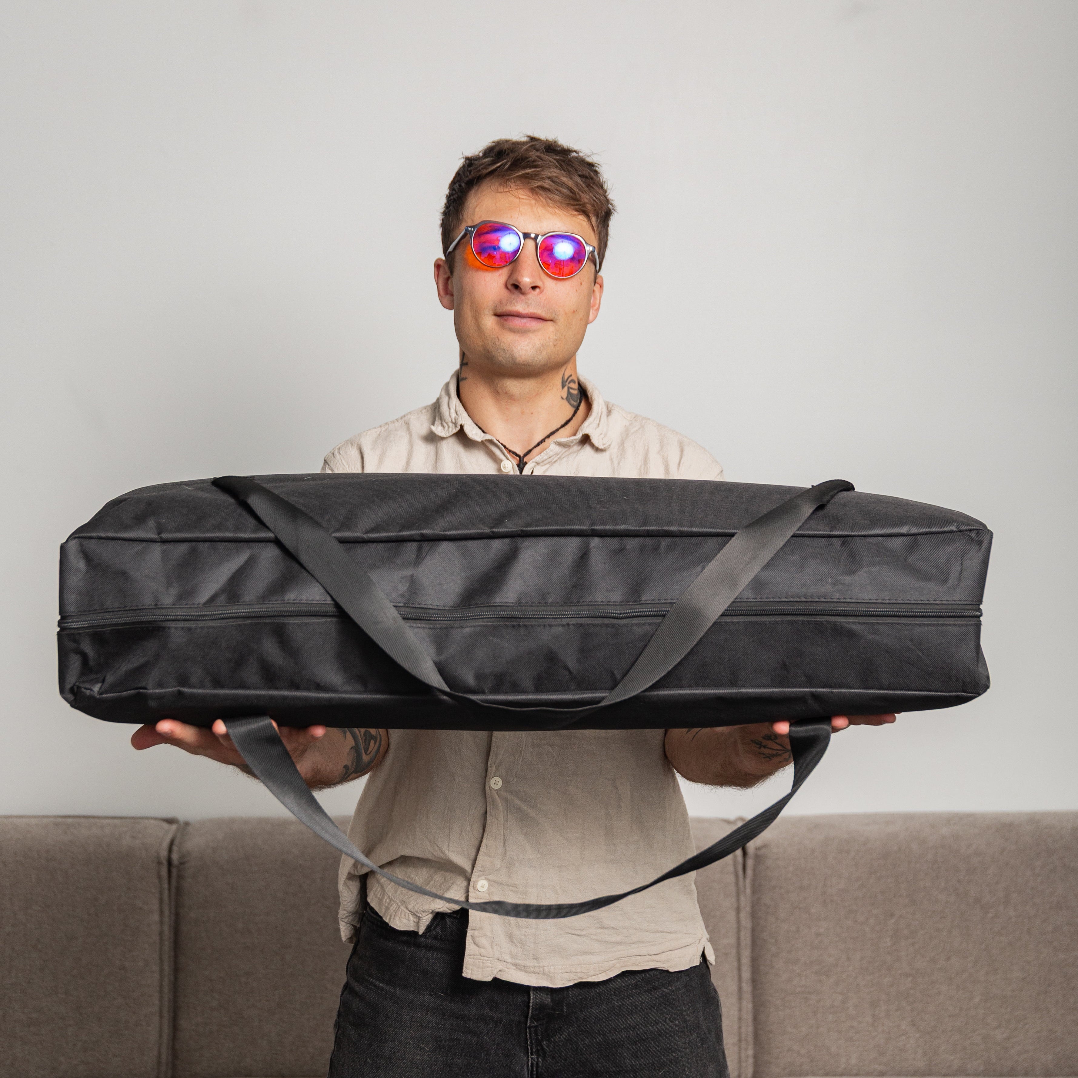 Man holding a large black carrying case with an infrared sauna inside against a plain background