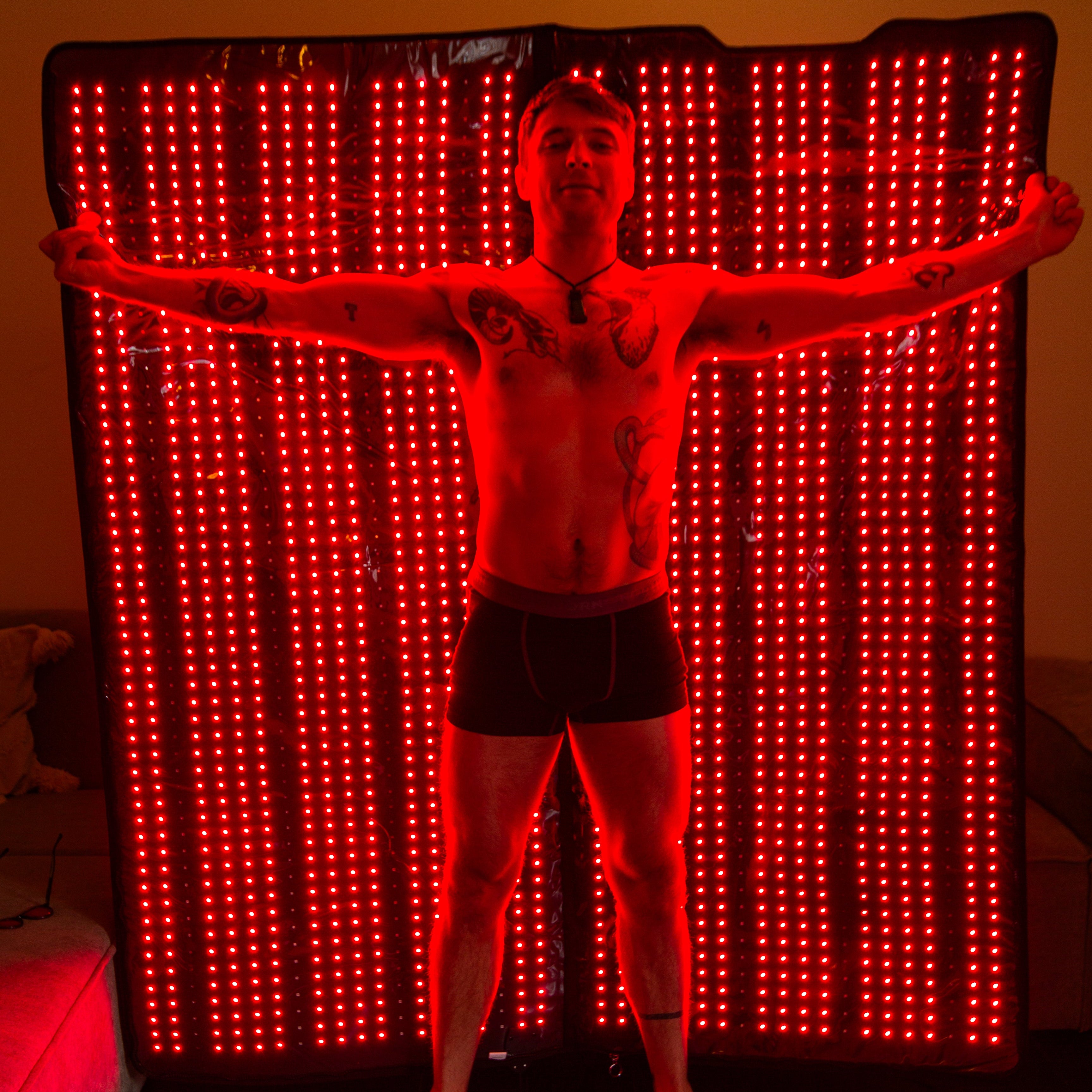Person posing in front of a red LED red light therapy full body blanket 