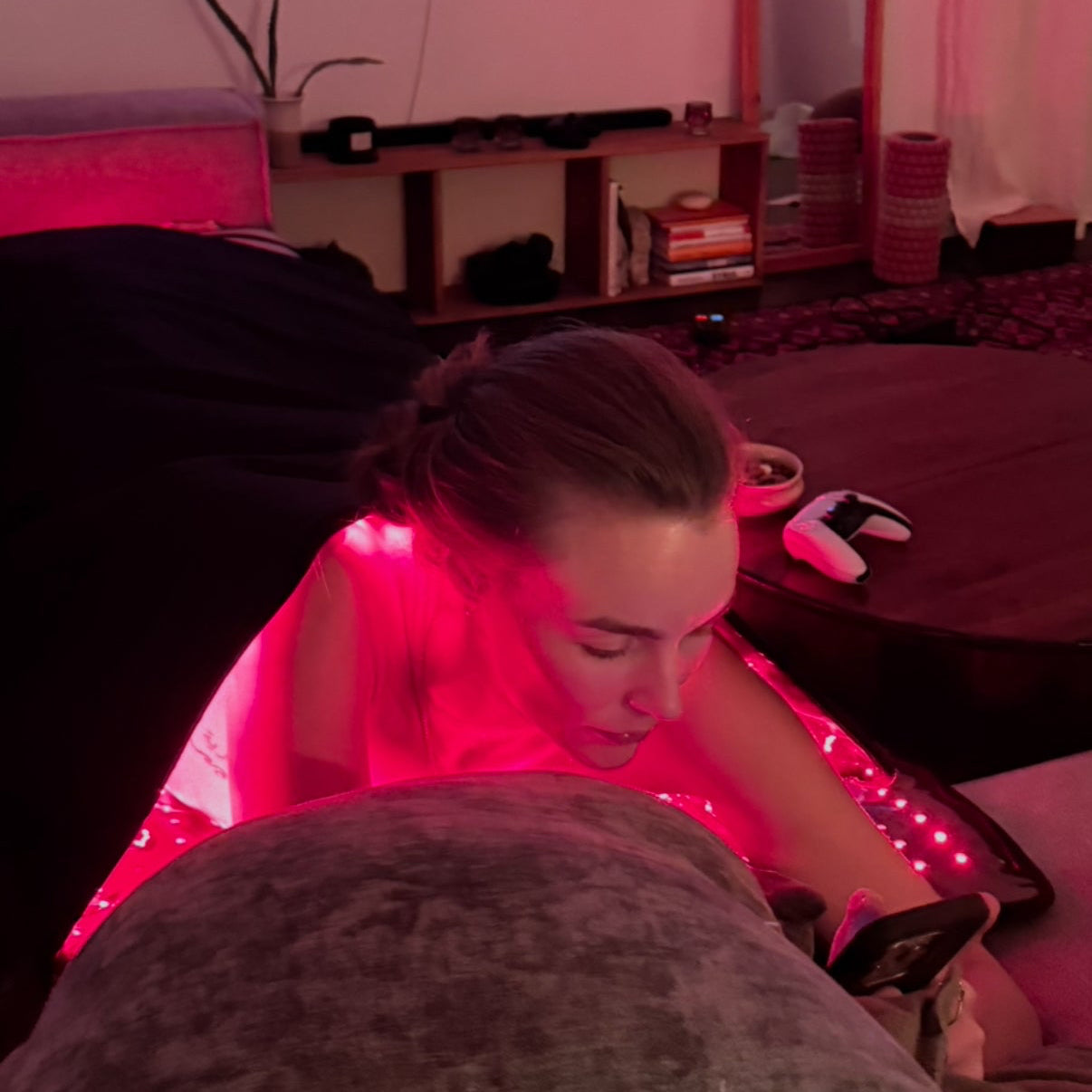 Person lying on a massage table with red light therapy blanket, TV in the background